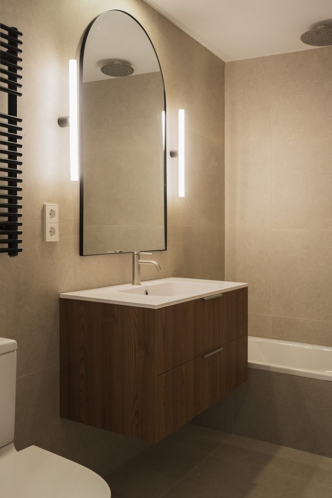 modern bathroom with warm elements like a big sink with wooden drawers, big mirror with lights on each side