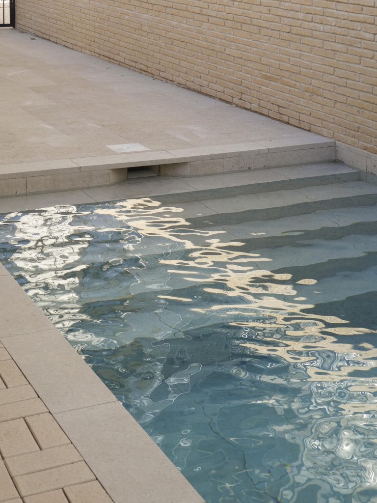 narrow swimming pool made from beige stones with blue water